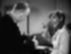 A woman in striped robe gestures with a pen at a man in a suit, indoors. They are engaged in a serious conversation. Black and white image. Jean Arthur goes over the morning routine with Charles Coburn who maps it with his hands in the classic Hollywood romantic comedy film rom-com movie 1940s "The More the Merrier".