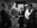 People in formal attire indoors, a couple kissing passionately. Others watching, one holding a book. Background with framed pictures and books. Harry C. Bradley, William Powell, and Bodil Rosing watch Jean Harlow and Spencer Tracy kiss in the Hollywood film screwball 1930s comedy classic movie “Libeled Lady”