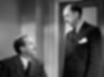 Two men in suits, one seated and looking up, the other standing, in a room next to a door. Black and white, serious expressions. Jame Seay and Porter Hall in the classic movie Hollywood holiday Christmas Santa Claus film "Miracle on 34th Street"