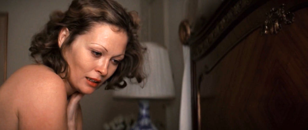 A woman with short hair looks down, appearing concerned. She's indoors near a wooden dresser and a lamp with a blue and white vase base. Faye Duanway in the classic 1970s Hollywood movie neo-film noir detective thriller story "Chinatown"