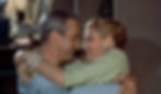 A smiling man and woman embrace closely in a warm room. She wears pearl jewelry, and they seem content and affectionate. James Jimmy Stewart and Grace Kelly are in love in the Alfred Hitchcock classic Hollywood film suspense voyeuristic movie "Rear Window" Peeping Tom