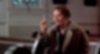 Elderly woman in a coat gestures with a raised finger, smiling in a church setting with wooden pews and stained glass. Warm lighting. Ruth Gordon spots Harold in the cult classic movie 1971 Hollywood film "Harold and Maude"