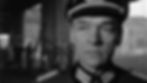 Black and white image of a stern military officer in uniform indoors. Background shows blurred figures and a ladder, creating a tense atmosphere. Paul Scofield stars in a scene from the 1964 action adventure movie World War II WWII film about the Nazis and stolen art, "The Train"