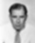 Black and white portrait of a man in a white shirt and tie, looking serious. Plain background, no visible text. Hollywood film director, screenwriter portrait photo of younger George Seaton