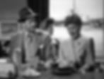 Man and woman in vintage attire sit at a diner counter; man looks concerned, woman appears upset. Vintage decor and airport visible behind them. Joel McCrea and Jean Arthur have breakfast in a diner in the classic Hollywood romantic comedy film rom-com movie 1940s "The More the Merrier".