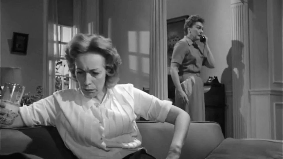 Two women in a room; one sits looking upset with a drink, while the other is on a phone. Shadows cast on a wall in a tense scene. Eileen Heckart and Nancy Kelly in the cult classic film melodrama horror thriller Hollywood movie "The Bad Seed"