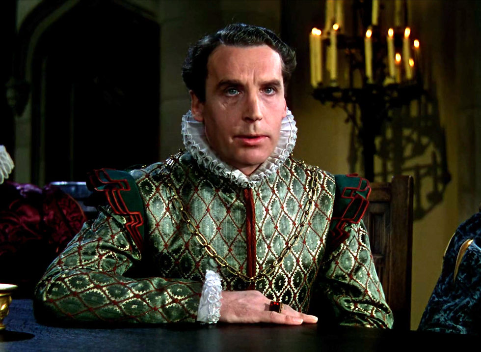 Serious man in ornate Renaissance dress sits at a table in a dim candlelit room, staring ahead. Henry Daniell in costume by Orry-Kelly in the classic Hollywood costume drama 1939 movie about Queen Elizabeth I and the Earl of Essex in "The Private Lives of Elizabeth and Essex"