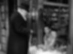 Elderly man with cane near shop window labeled "ACCESSORIES." Younger man inside arranges decorative items. Black-and-white street scene. Edmund Gwenn and Robert Gist arrange reindeer in a story window display in the classic movie Hollywood holiday Christmas Santa Claus film "Miracle on 34th Street"