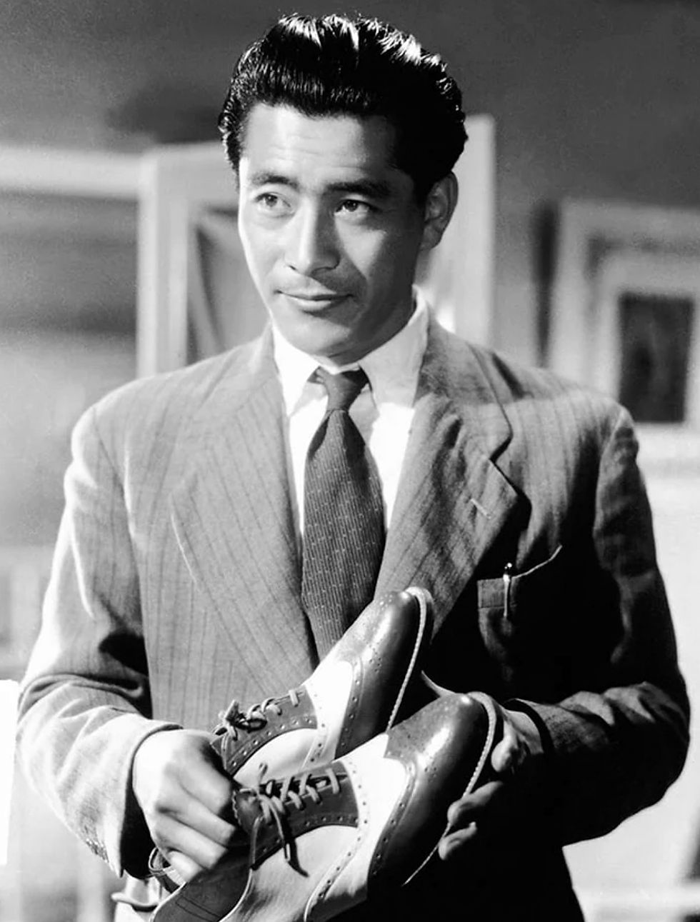 portrait of young Japanese movie star icon actor Toshirô Mifune holding shoes