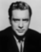 Black and white portrait of a man in a suit. He has slick, wavy hair and a serious expression. Plain background enhances focus on face. Portrait photo of Hollywood film actor movie star young Edmond O'Brien