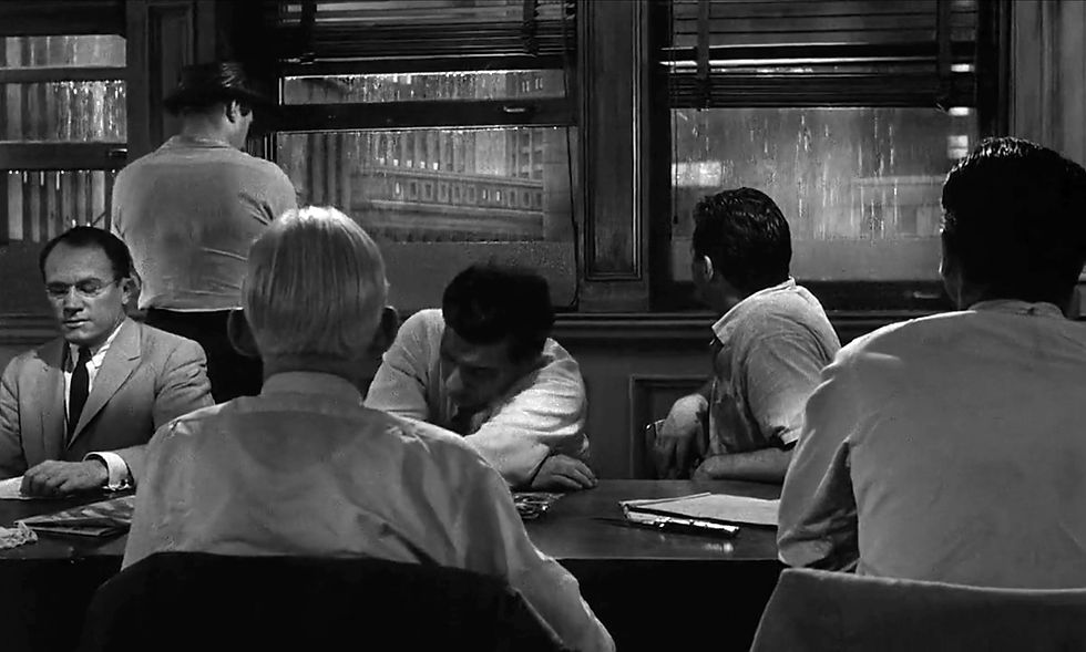 Black-and-white image of six men in a room. Four are seated around a table with papers, one stands by a rainy window, another looks outside. Serious mood. E.G. Marshall and the other jurors in the classic movie Hollywood courtroom drama film "12 Angry Men" twelve