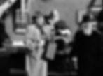 A woman in a coat with a bottle stands beside a seated Santa figure and a bearded man. They're outdoors, near a festive house facade. Maureen O'Hara, Percy Helton, Edmund Gwenn in the classic movie Hollywood holiday Christmas Santa Claus film "Miracle on 34th Street"