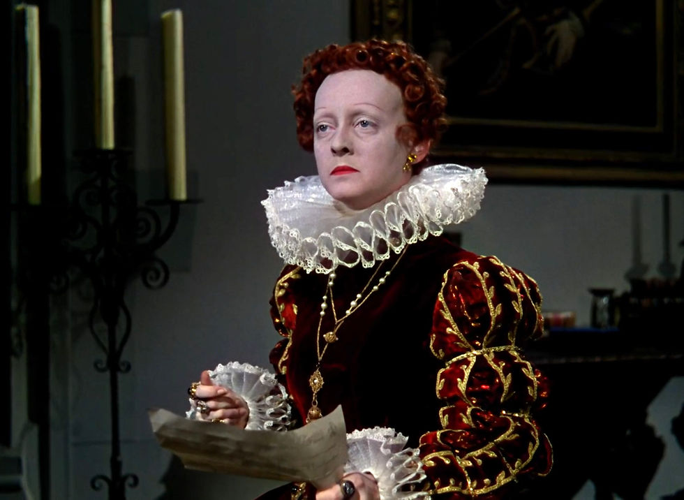 Pale woman in ornate red-and-gold Renaissance dress reads a paper in a dim room, her expression stern and somber. Bette Davis as Queen Elizabeth I 1 in costume by Orry-Kelly in the classic Hollywood costume drama 1939 movie about Queen Elizabeth I and the Earl of Essex in "The Private Lives of Elizabeth and Essex"