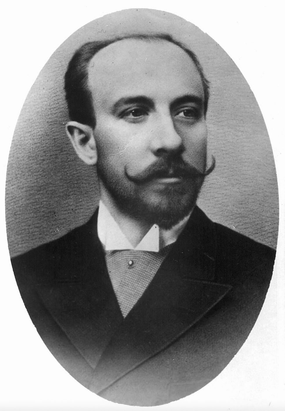 Black and white portrait of a man with a mustache and beard, wearing a formal suit. He has a calm expression. Oval-shaped frame. Portrait photo of French early film director producer special effects inventor magician Georges Méliès