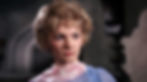 Woman with blond hair and blue eyes wearing a translucent blue scarf, looks serious in a dimly lit room with gray stone walls. Barbara Loden is the oversexed sister in the classic 1960s Hollywood film romance movie about sex and repression, "Splendor in the Grass"
