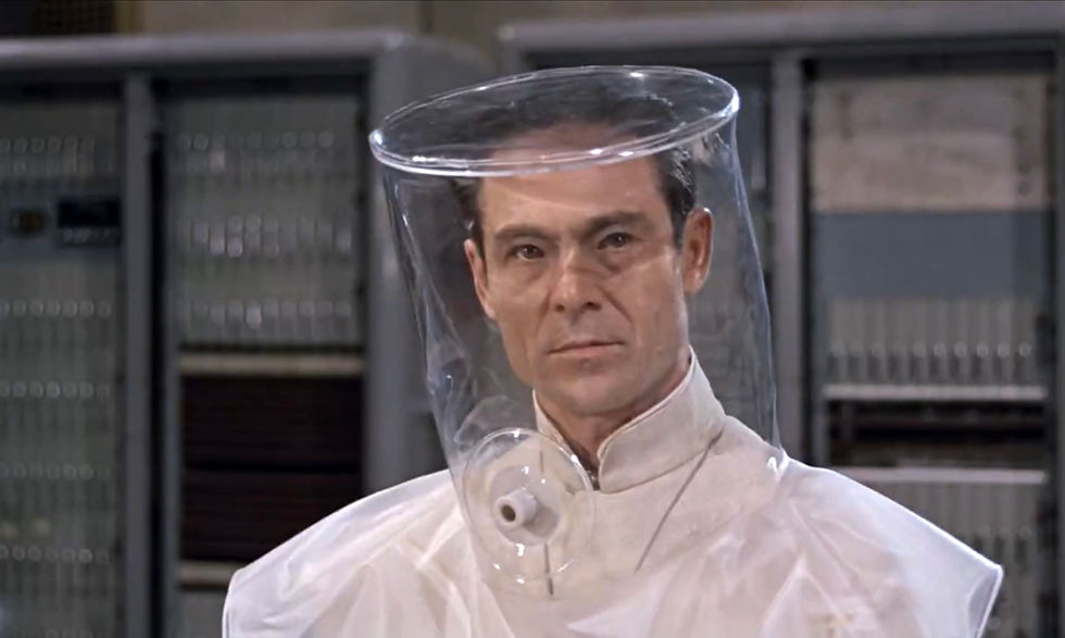 Serious man in a clear plastic hood and white suit stands in a lab-like room with gray equipment in the background. Joseph Wiseman is the evil mad scientist in the first classic James Bond movie espionage spy thriller 007 film 1962 "Dr. No"