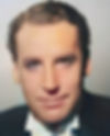 Close-up portrait of a man in a black tuxedo and bow tie, softly lit against a plain gray background with a calm expression. Color portrait photo of Hollywood movie star film actor TV villain young Henry Daniell