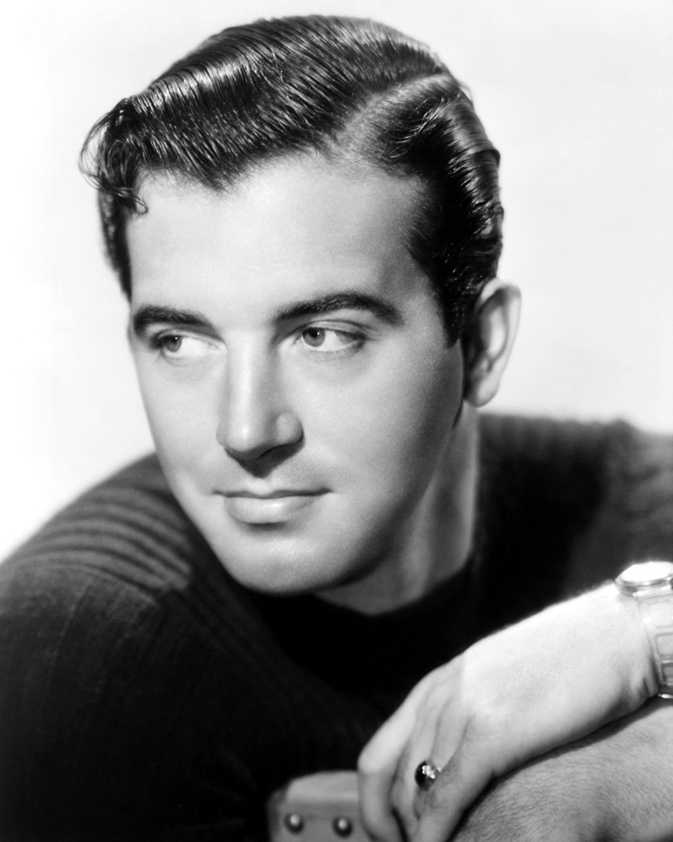 Black and white portrait of a man with slicked-back hair, wearing a dark sweater, resting his chin on his arms. He appears thoughtful. portrait of young film actor Hollywood movie star John Payne