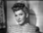 Woman with styled hair and striped blouse gazes with a slight smile. Black and white image with soft shadows on a patterned wall. Jean Arthur stars in the classic Hollywood romantic comedy film rom-com movie 1940s "The More the Merrier".