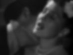 Black and white image of a woman with closed eyes, wearing pearls and a flower in her hair, as a man behind her leans in close, creating an intimate mood. Joel McCrea kisses Jean Arthur's neck on the stairs in the classic Hollywood romantic comedy film rom-com movie 1940s "The More the Merrier".