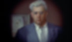 Man with gray hair and glasses in a suit and tie looks serious. Background features blurred painting and darkened corners. Raymond Burr plays a traveling salesman in the Alfred Hitchcock classic Hollywood film suspense voyeuristic movie "Rear Window" Peeping Tom