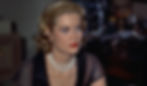 Woman with short blonde hair, wearing a black dress and pearl necklace. She appears serious against a blurred dark background. Grace Kelly in pearls in the Alfred Hitchcock classic Hollywood film suspense voyeuristic movie "Rear Window" Peeping Tom