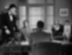 Man in tuxedo stands at a desk in an office setting, observed by seated men and a woman. One man reads a newspaper. Mood is tense. Richard Gaines, Joel McCrea, Charles Coburn and Jean Arthur at the FBI office in the classic Hollywood romantic comedy film rom-com movie 1940s "The More the Merrier".