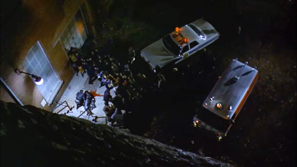 Nighttime rescue scene: ambulances and responders crowd outside a building, lights flashing in the dark. A death on the Georgetown stairs in the scariest movie of all time, classic horror film about the devil and possession, 1973 "The Exorcist".
