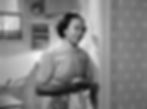Woman in a vintage kitchen smiles warmly, holding a cloth. She wears a checkered dress. The background has patterned wallpaper. Black and white image. Theresa Harris as Cleo in the classic movie Hollywood holiday Christmas Santa Claus film "Miracle on 34th Street"