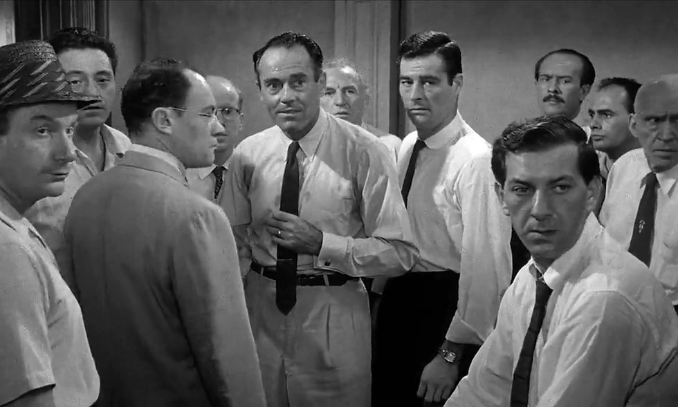 A group of men in ties and shirts stand in a room looking serious and contemplative. The setting is monochrome with a tense atmosphere. Jack Warden, Edward Binns, E.G. Marshall, John Fiedler, Henry Fonda, Ed Begley, Robert Webber, Jack Klugman, George Voskovec, Martin Balsam, and Joseph Sweeney star in the classic movie Hollywood courtroom drama film "12 Angry Men" twelve