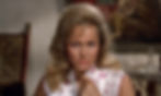Close-up of a stern blonde woman in a pink floral satin top, pointing at herself indoors with a blurred room behind her. Ursula Andress stars in the first classic James Bond movie espionage spy thriller 007 film 1962 "Dr. No"