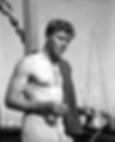 Shirtless man with a towel over shoulder leans on boat rail, holding a cigarette. Clear sky and ship’s mast in background. Calm mood. Candid shirtless photo of younger bare chested Hollywood movie star film actor producer icon tough guy Burt Lancaster