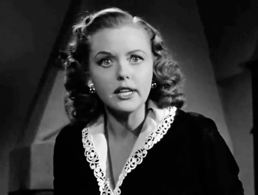 Woman with curly hair and intense expression, wearing a dark dress with lace collar, in a dimly lit setting. Black and white image. Martha Stewart tells us the story of the book as the hat check girl in the classic Hollywood movie romance Nicholas Ray film noir "In a Lonely Place"