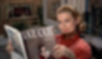 Woman in red blouse reading Bazaar magazine by an open window. Background shows blurred buildings. Calm and focused expression. Grace Kelly stars as a fashion buyer model in the Alfred Hitchcock classic Hollywood film suspense voyeuristic movie "Rear Window" Peeping Tom