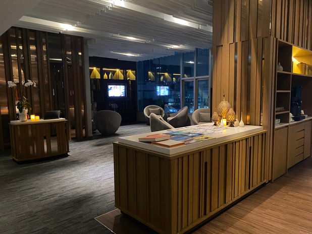 Modern hotel lounge with wooden slat walls, white countertops, gray armchairs, and warm lighting at night.