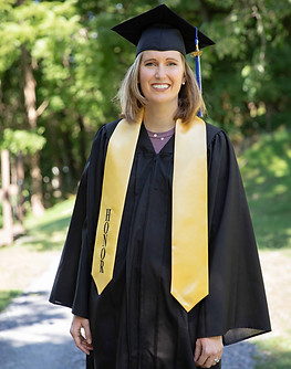 Autumn Carter, founder of Wellness in Every Season, wearing a graduation cap and gown with a gold honor stole, standing outdoors on a sunny day with a lush green background, celebrating her academic achievement.