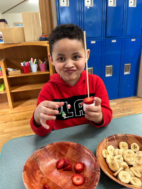 Preschoolers using bananas and sliced strawberries to fruit kabo's in class.