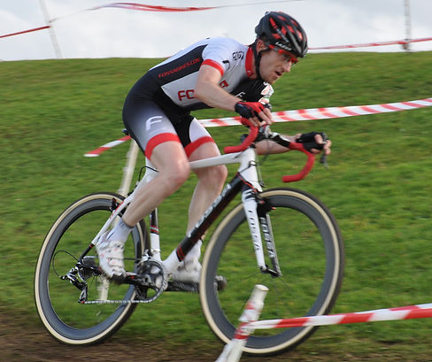 Andrew Naylor riding in a cyclocross race for Fossa Racing. He is traversing a grassy camber and looks focussed.