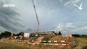 Baustelle mit Kran und Gerüst unter wolkigem Himmel; oben links steht LAGO VISTA, rechts ein Vogel-Logo.
