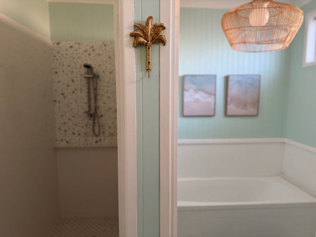 the main bathroom there is a room to the left that is the shower with a door and the room to the right has a bath this room has nice energy , art work on the wall and a large cane wicker light fitting