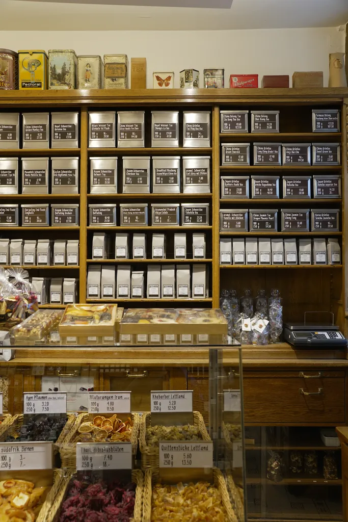 Wall of teas and dried fruits at Schwarzenbach Zurich, with neatly arranged black tins and hand-written labels in a cozy, old-school wooden shop setting.