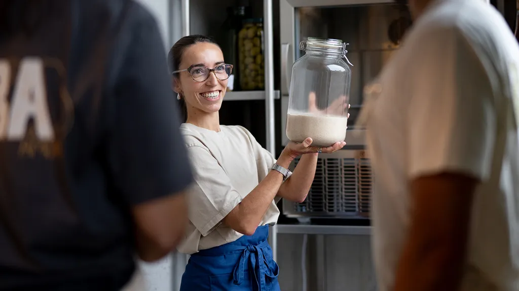 Smiling team member at ALBA Zurich holding a jar of sourdough starter, showcasing the behind-the-scenes passion — highlighted by BYCA Zurich.