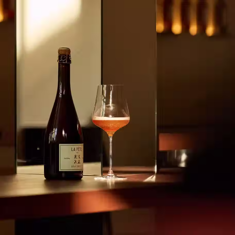 •	EN: “La Fête sans Deux Frères bottle with a poured glass of alcohol‑free sparkling rosé on a bar in warm ambient light.”