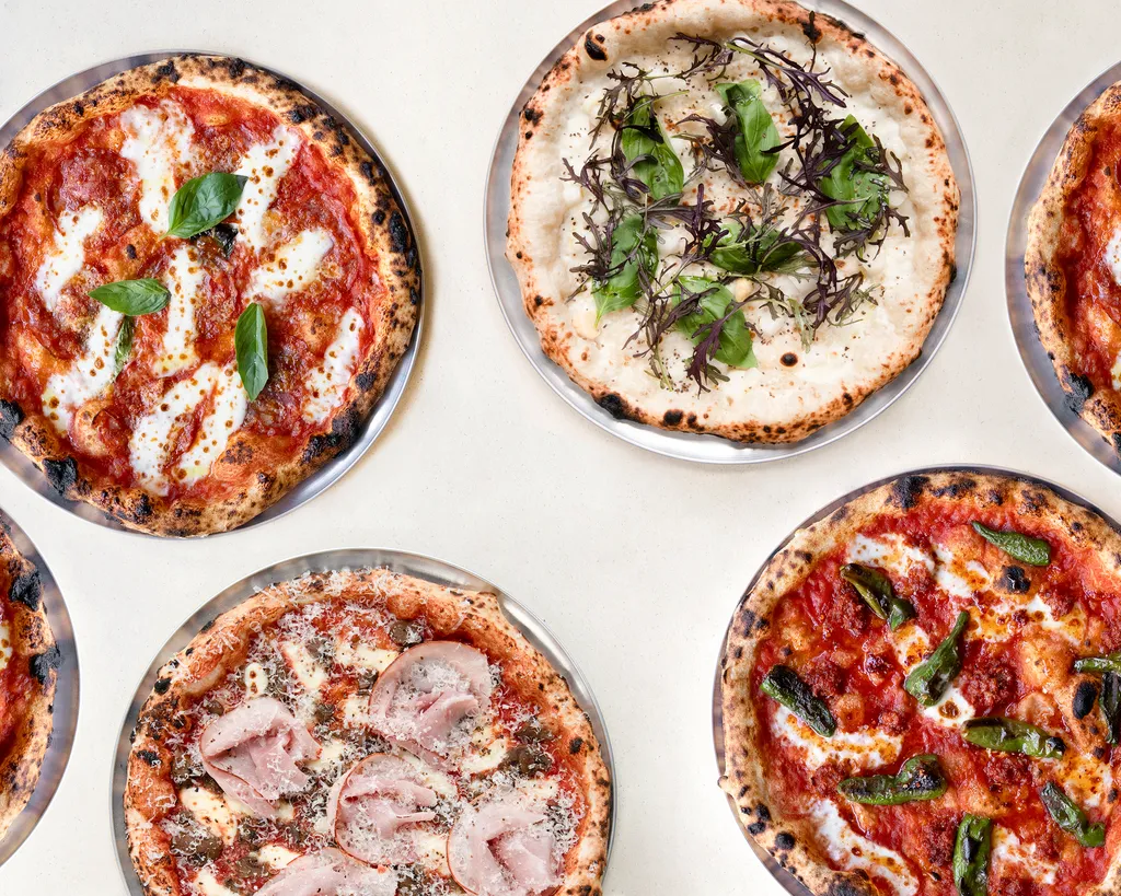A colorful selection of pizzas with different toppings on metal plates, photographed from above at ALBA Zurich — featured by BYCA Zurich.