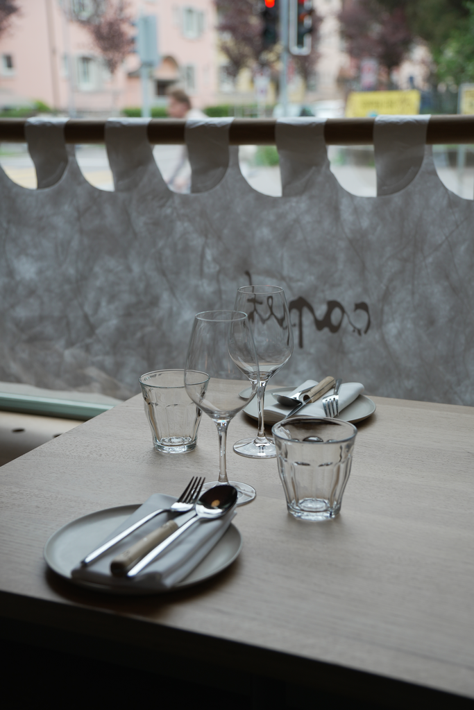 Beautifully set table at Capet Zurich with elegant glassware and cutlery, next to a window with soft daylight.