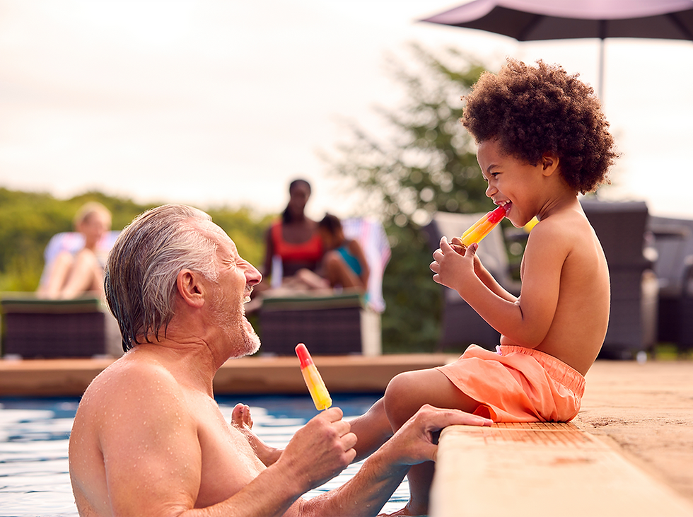 Man and child enjoying popsicles by a pool. The man is in the water, smiling at the child seated on the edge. Sunny, relaxed atmosphere.