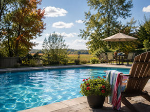 Backyard pool scene with leave starting to change color in the background and a lawn chair with a towel on it and patio flowers.