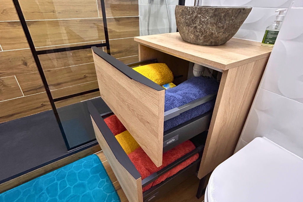 alt="Meuble mural de salle de bain avec vasque en pierre de rivière, serviettes de douche et gants de toilette fournis dans les tiroirs"