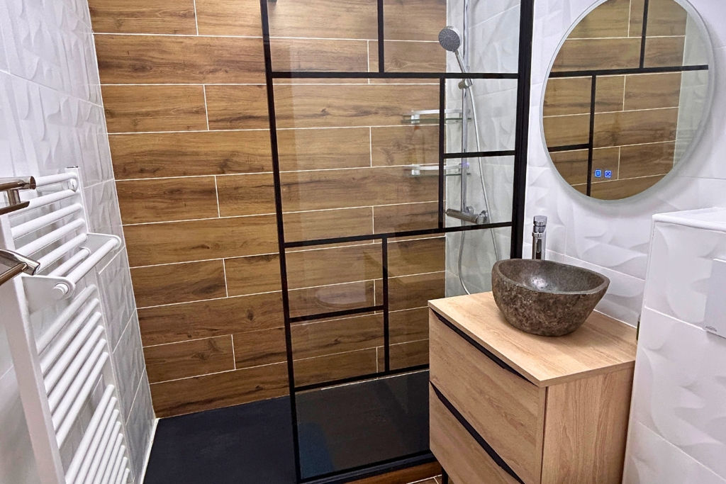 alt="Salle de bain avec douche à l’italienne, meuble mural, toilettes suspendues, radiateur électrique et miroir LED anti-buée"