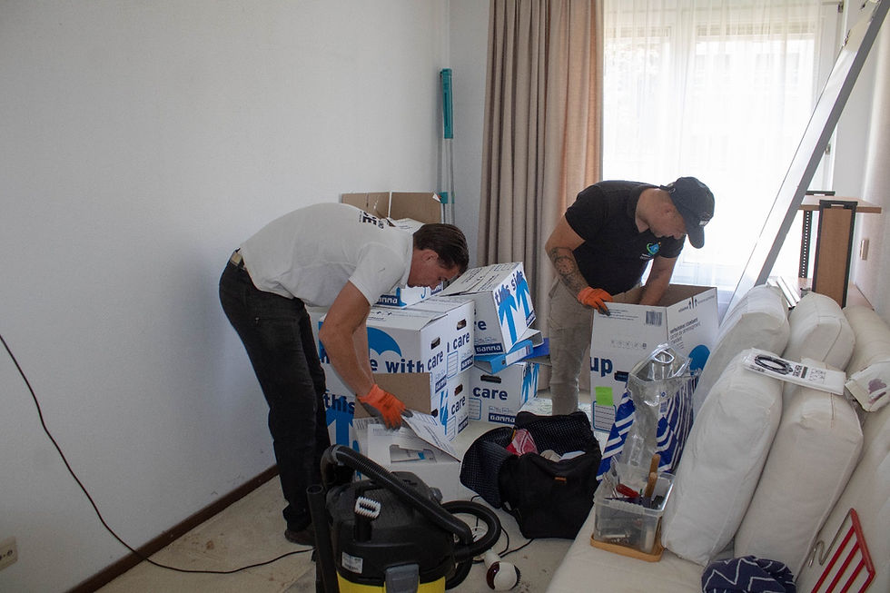 Twee mannen pakken dozen uit in een lichte kamer, met een stofzuiger.